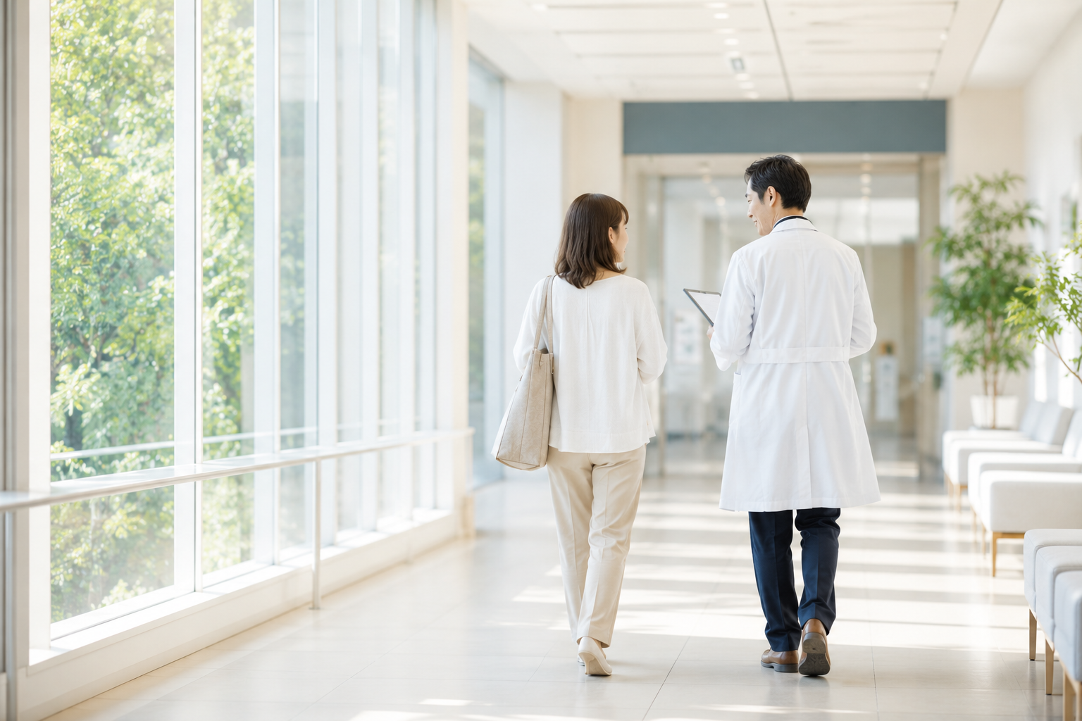 自然光が差し込む病院の廊下で、医師と患者が並んで歩きながら対話している様子。診断後も続く長期的な疾患管理をイメージした写真